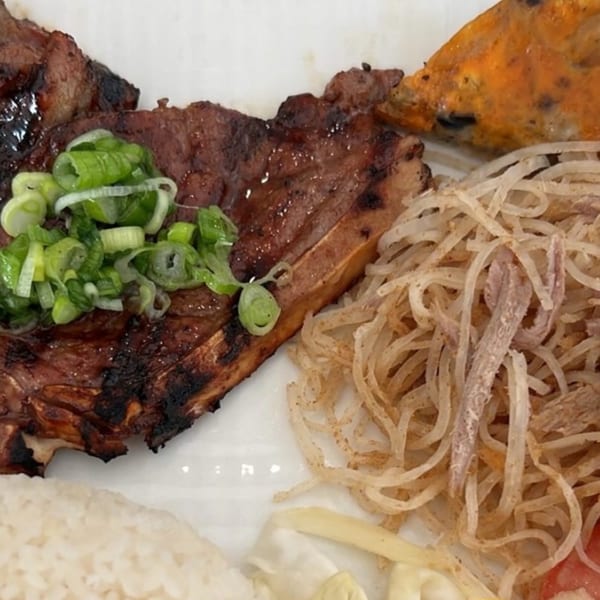 Grilled pork chop topped with green onions, served with rice, noodles, and a fried egg.