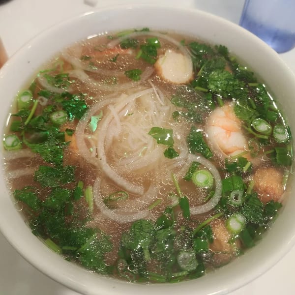 A close-up of a bowl of Pho Viet Cali's pho with noodles, shrimp, and fresh herbs.