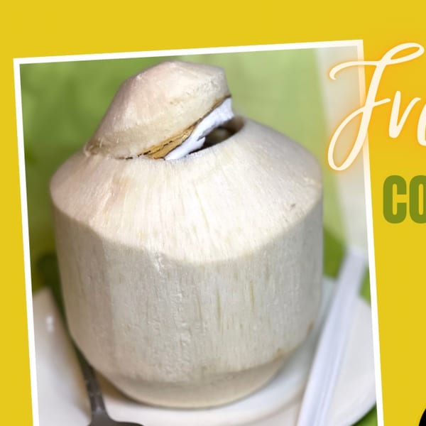 A fresh young coconut, with its top cut open, served with a straw on a white plate.