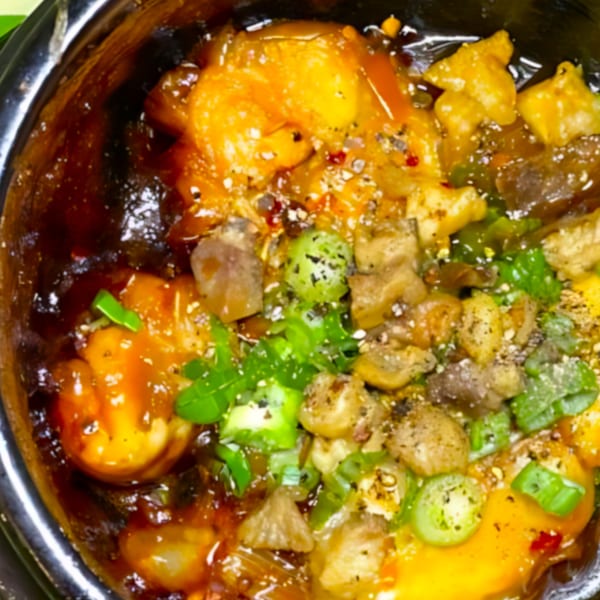Close-up of a Vietnamese dish with shrimp, meat, and green vegetables in a rich sauce.