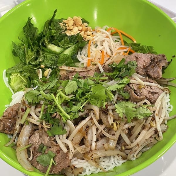 A vibrant green bowl filled with Vietnamese vermicelli noodles, beef, fresh herbs, and bean sprouts.