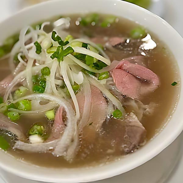 Close-up of a bowl of Pho Viet Cali's Vietnamese pho with thinly sliced beef, onions, and green onions.