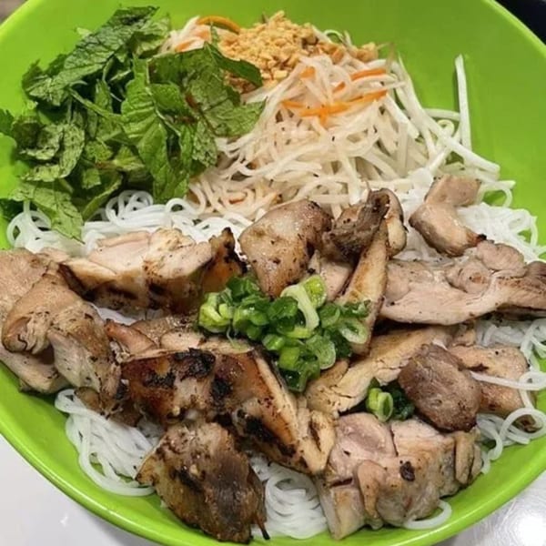 A vibrant green bowl of Vietnamese vermicelli noodles with grilled chicken, mint, and crushed peanuts.