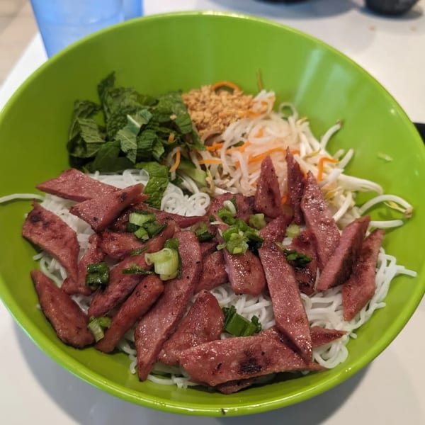 A vibrant green bowl filled with Vietnamese vermicelli noodles, grilled pork, fresh mint, and pickled vegetables.