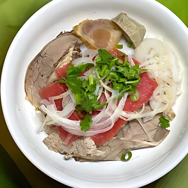A white bowl filled with various cuts of meat, onions, and cilantro, a Vietnamese dish.