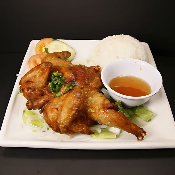 Whole roasted chicken with rice, sliced tomatoes, cucumbers, and a side of dipping sauce.