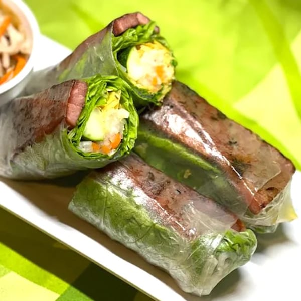 Four fresh Vietnamese spring rolls with meat, lettuce, and vegetables on a white plate.