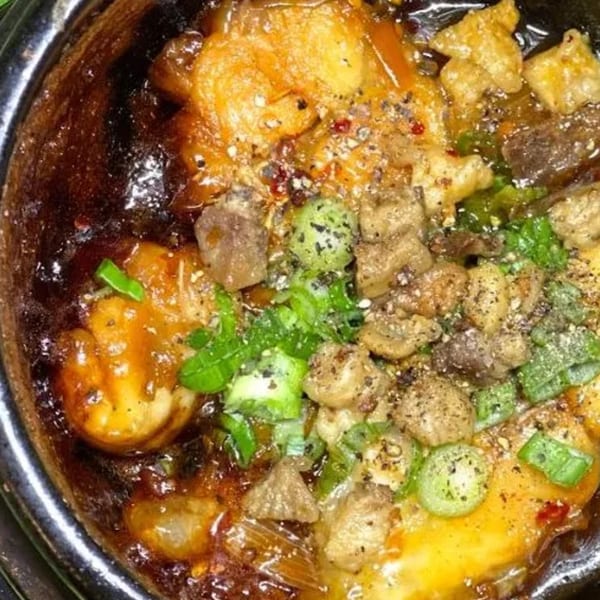 Close-up of Vietnamese clay pot dish with shrimp, pork, and green onions.