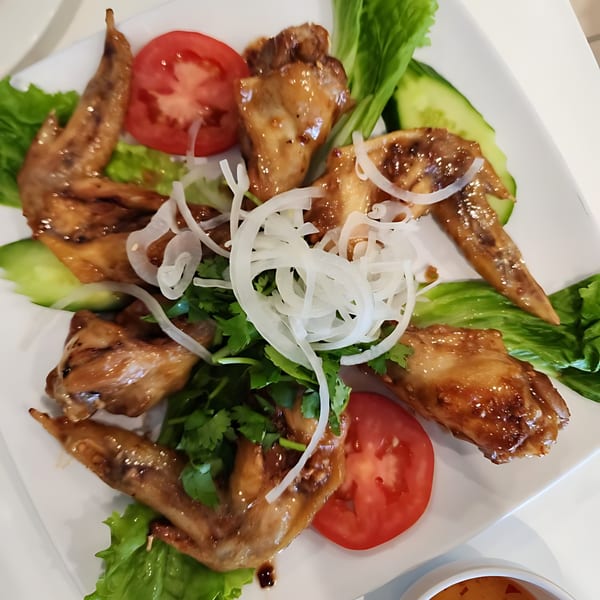 Vietnamese glazed chicken wings with sliced tomatoes, cucumbers, lettuce, cilantro, and onions.