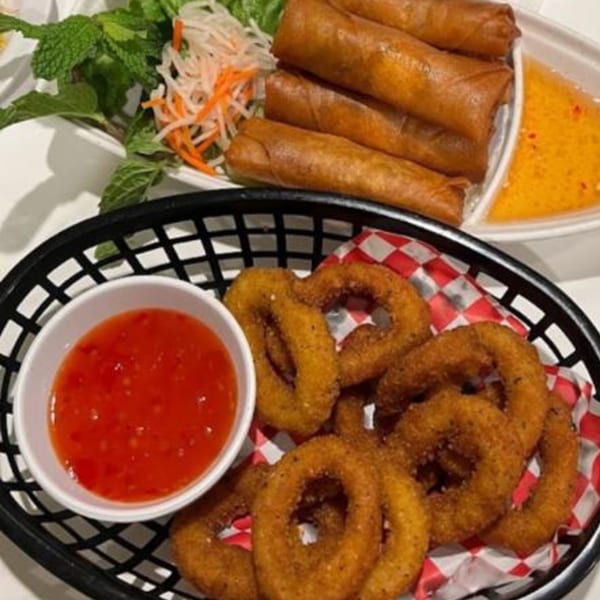 Crispy Vietnamese spring rolls with dipping sauce, alongside a basket of golden onion rings and sweet chili sauce.