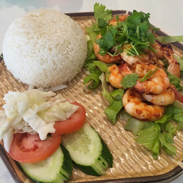 Vietnamese grilled shrimp with rice, lettuce, tomatoes, cucumbers, and cabbage on a woven plate.