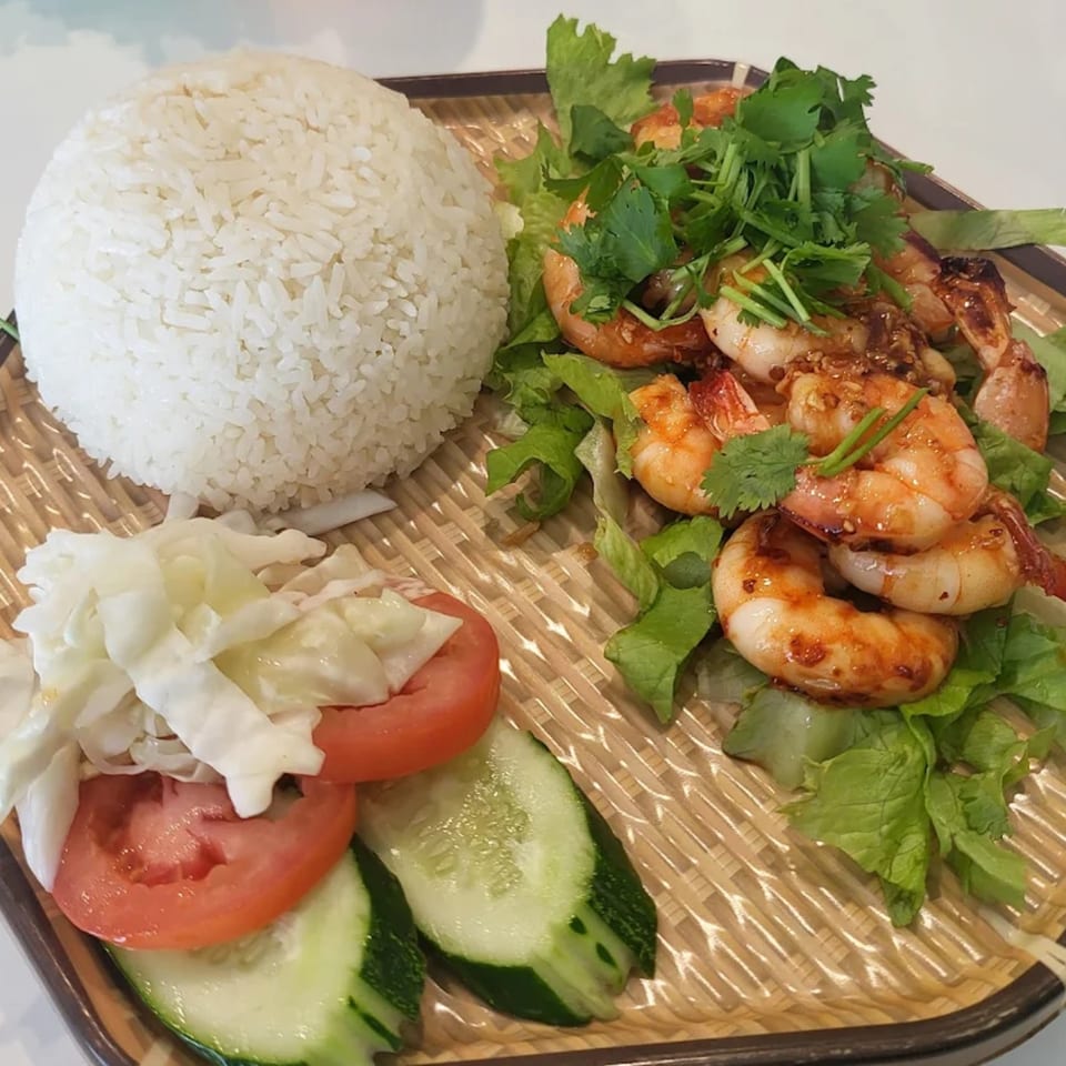 Vietnamese grilled shrimp with rice, lettuce, tomatoes, cucumbers, and cabbage on a woven plate.