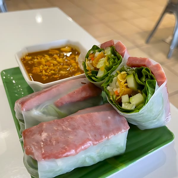 Fresh Vietnamese spring rolls with pink meat and vegetables, served with a side of peanut sauce.
