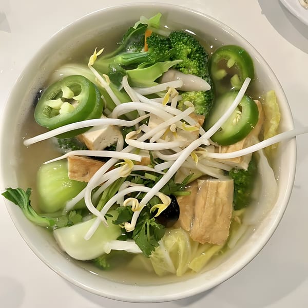 A bowl of Pho Viet Cali's vegetarian pho, brimming with fresh broccoli, bok choy, tofu, and bean sprouts.