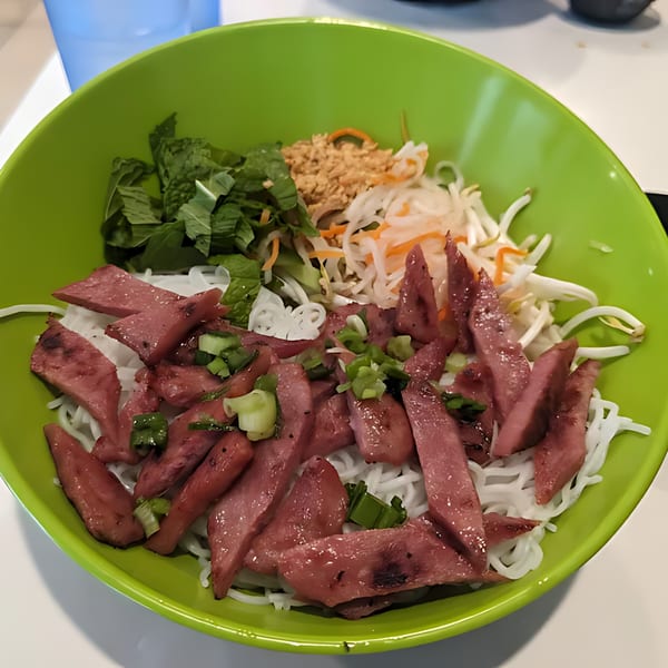 Vietnamese vermicelli noodle bowl with sliced grilled pork, mint, peanuts, and pickled vegetables in a green bowl.