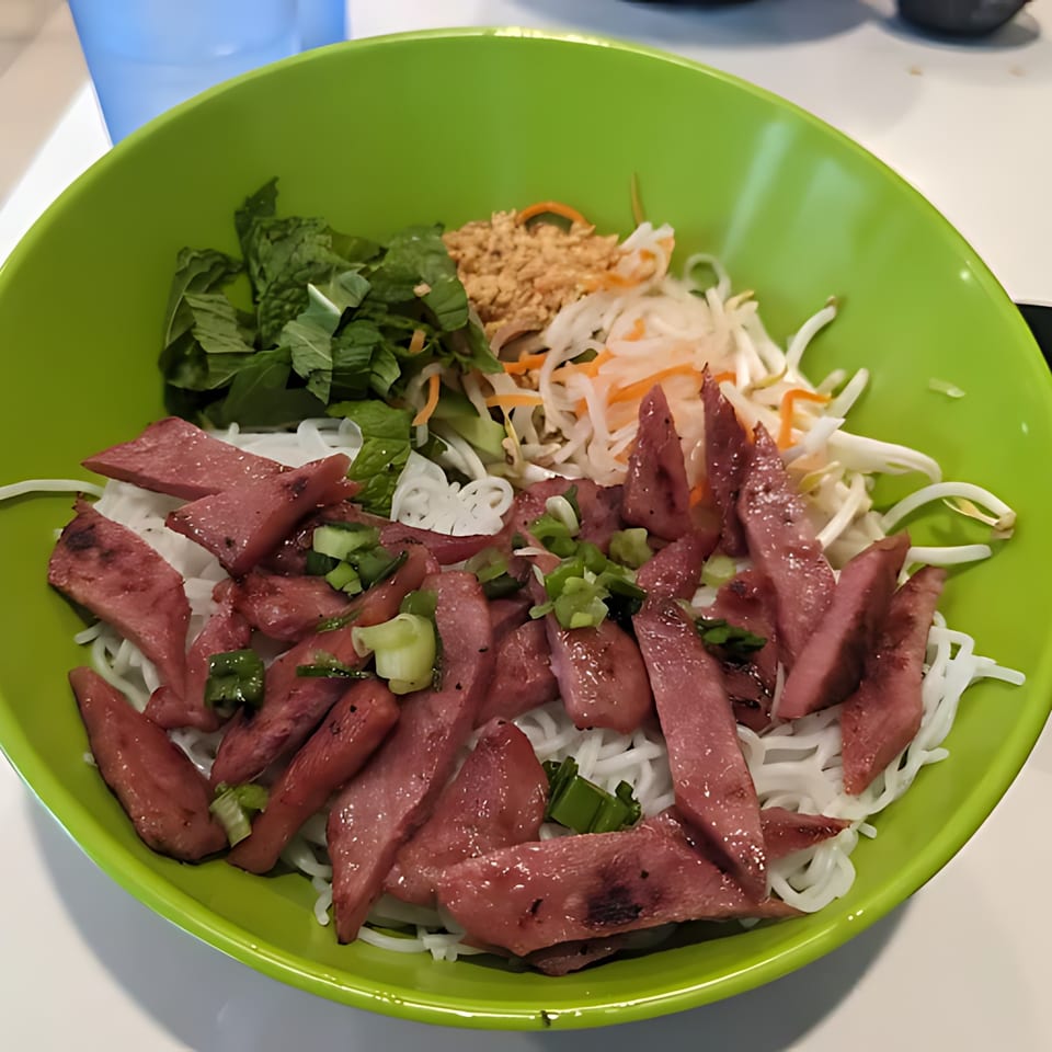 Vietnamese vermicelli noodle bowl with sliced grilled pork, mint, peanuts, and pickled vegetables in a green bowl.